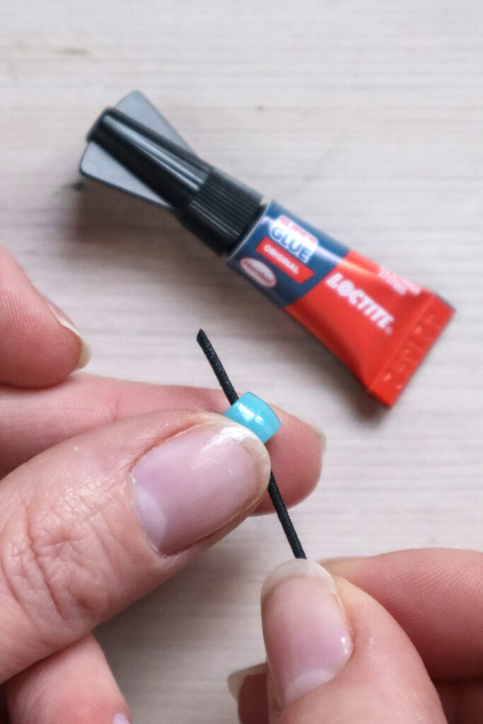 Comment réaliser un bracelet en perles - Enfiler une perle sur un élastique en tissu noir. Un peu de superglue a été ajoutée à la pointe pour aider