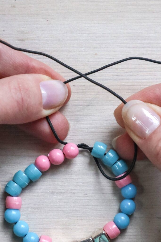 Comment faire un bracelet en perles - mains tenant l'extrémité droite de l'élastique sur la gauche