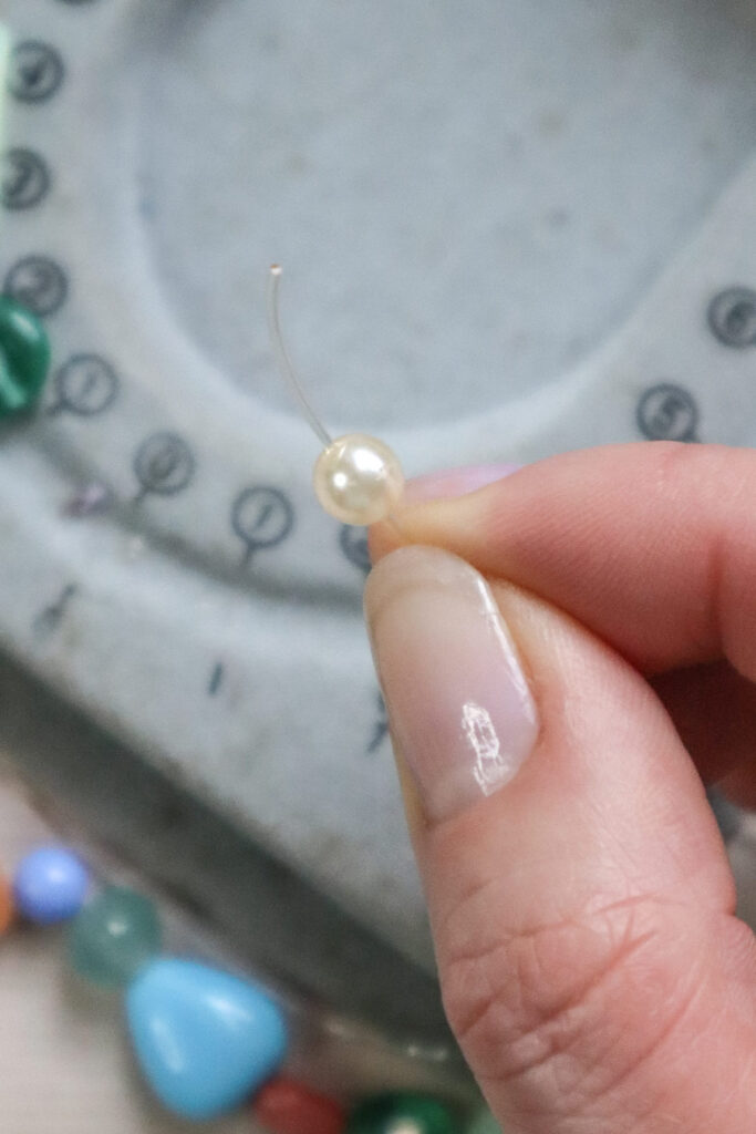 Comment faire un bracelet en perles - gros plan d'une main enfilant une perle sur un élastique magique extensible sans aiguille