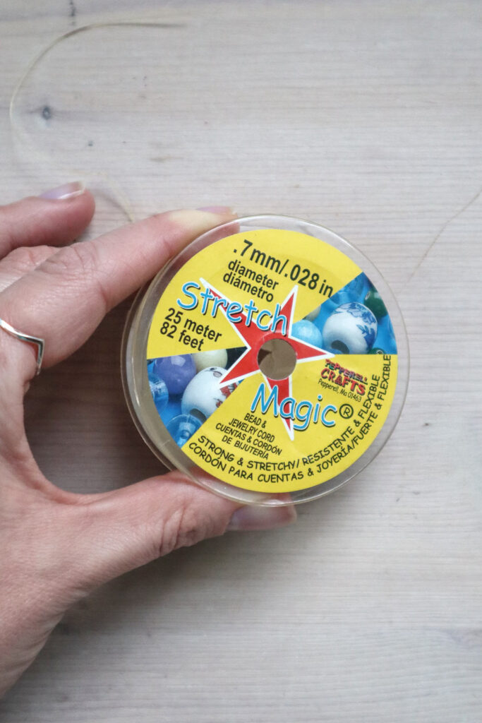 Comment fabriquer un bracelet en perles - mains tenant une bobine d'élastique en perles appelée Stretch Magic. 