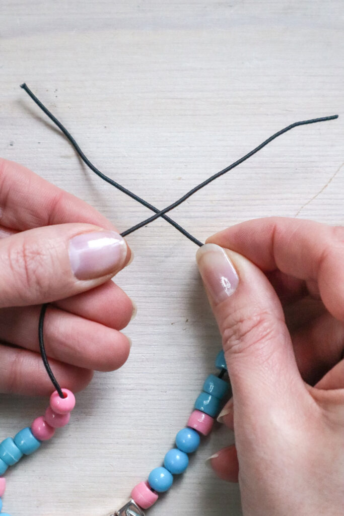 Comment fabriquer un bracelet en perles - mains tenant les extrémités d'un bracelet en perles, l'extrémité gauche passant par-dessus l'extrémité droite